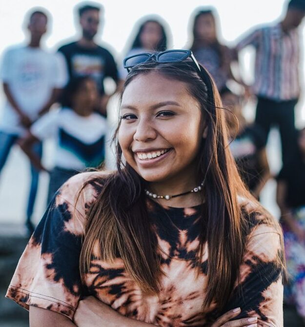 A cheerful woman stands with her arms crossed, surrounded by friends, showcasing happiness and camaraderie.